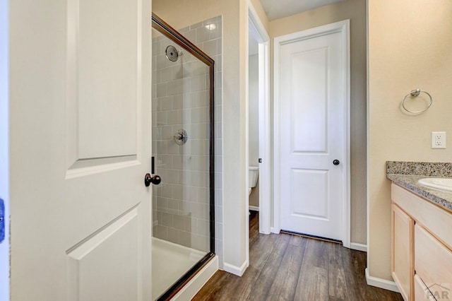 bathroom with tiled shower, wood finished floors, vanity, and baseboards