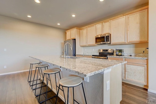 kitchen featuring a breakfast bar area, light brown cabinetry, appliances with stainless steel finishes, dark wood-type flooring, and a sink