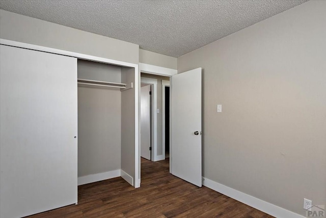 unfurnished bedroom featuring dark wood-type flooring, a closet, a textured ceiling, and baseboards