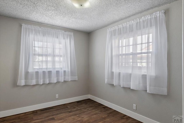 unfurnished room with baseboards, dark wood finished floors, and a textured ceiling