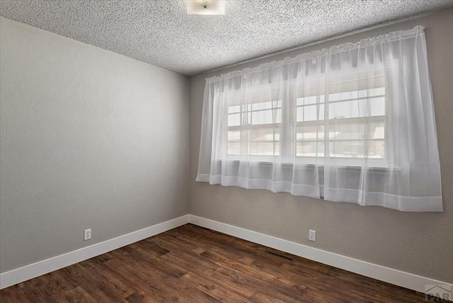 empty room with a textured ceiling, a textured wall, dark wood-type flooring, and baseboards