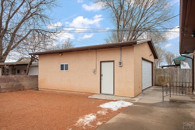 back of property with stucco siding, a detached garage, fence, and an outbuilding