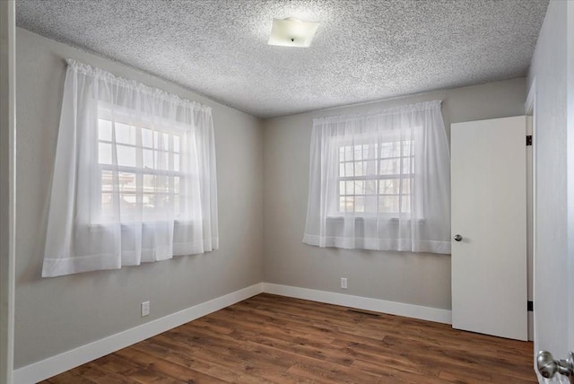 unfurnished room featuring a textured ceiling, baseboards, dark wood-style flooring, and a wealth of natural light