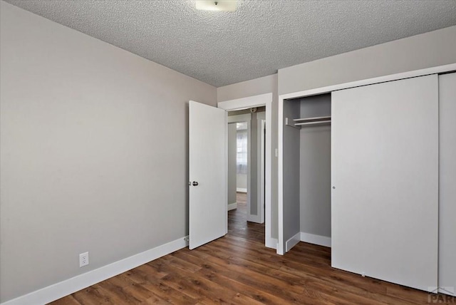 unfurnished bedroom featuring a textured ceiling, baseboards, dark wood finished floors, and a closet