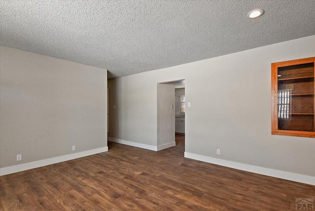 empty room featuring a textured ceiling, dark wood-style flooring, and baseboards