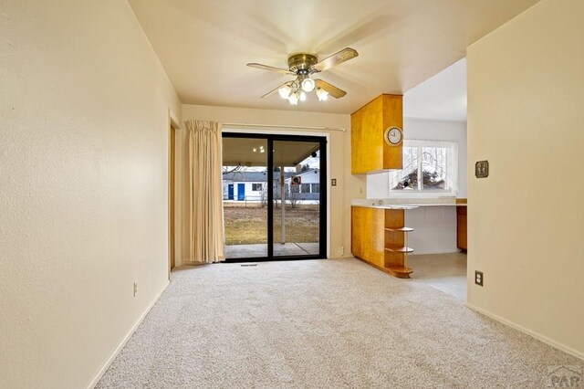 unfurnished living room featuring light colored carpet, ceiling fan, and baseboards