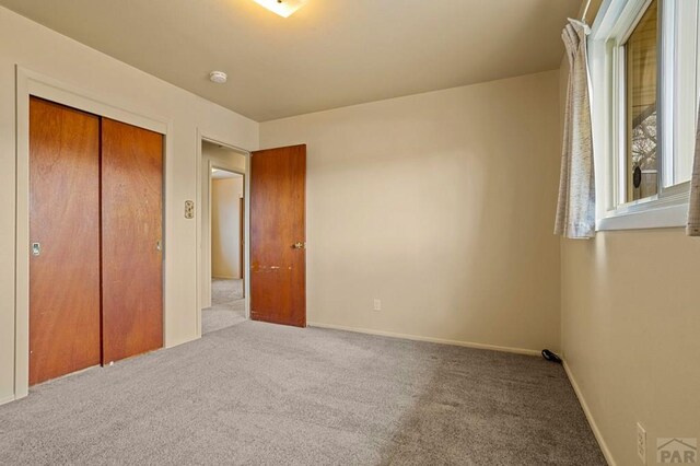 unfurnished bedroom featuring a closet, light carpet, and baseboards