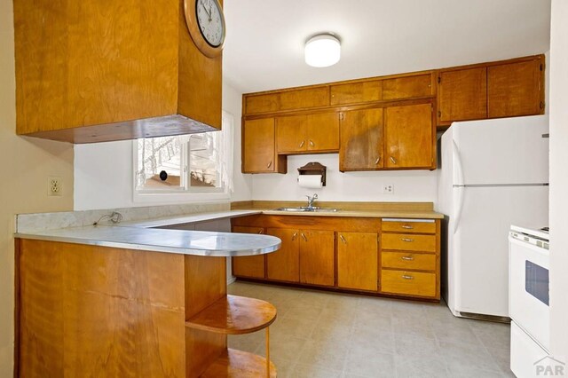 kitchen with white appliances, brown cabinetry, a peninsula, light countertops, and a sink