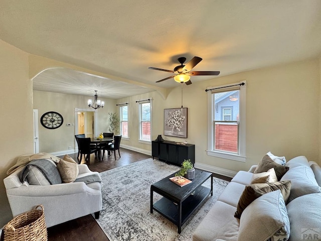 living area featuring baseboards, dark wood finished floors, arched walkways, and ceiling fan with notable chandelier