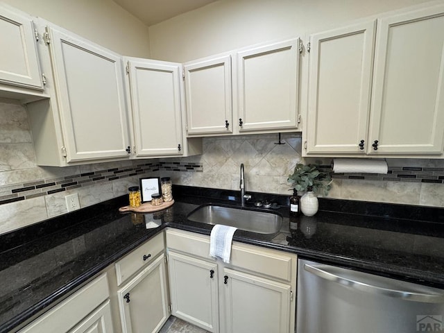 kitchen featuring backsplash, stainless steel dishwasher, white cabinetry, a sink, and dark stone counters