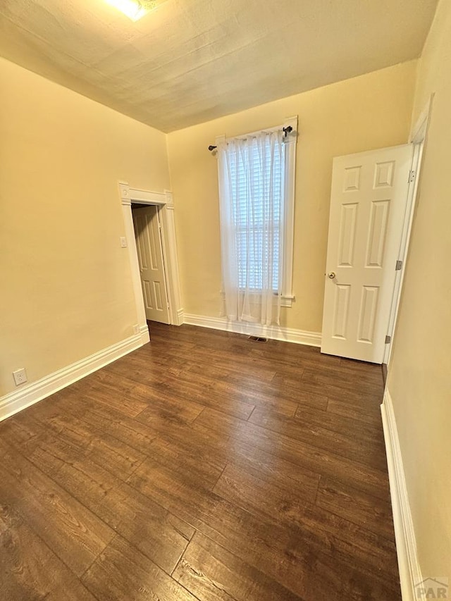 unfurnished room with dark wood-style flooring, visible vents, and baseboards