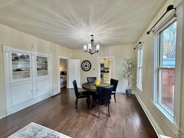 dining space featuring dark wood-type flooring, a chandelier, and baseboards