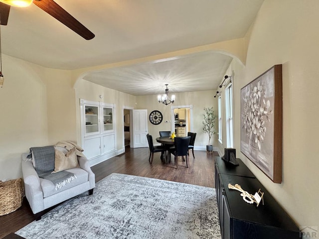 living area featuring arched walkways, dark wood-style flooring, baseboards, and ceiling fan with notable chandelier