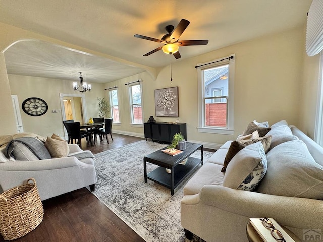 living room with dark wood-style floors, baseboards, arched walkways, and ceiling fan with notable chandelier