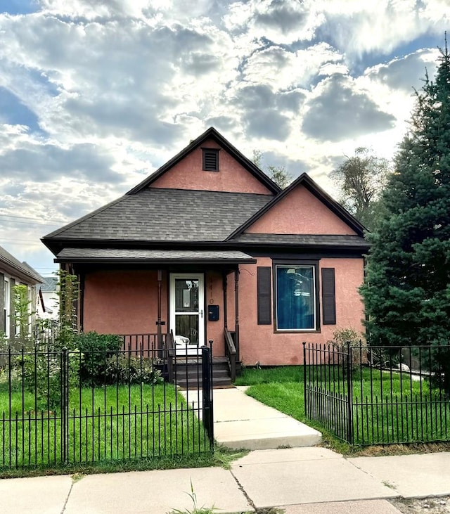 view of front of house with a fenced front yard, a shingled roof, a front lawn, and stucco siding