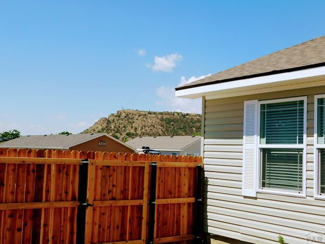 view of side of home with roof with shingles, fence, and a gate