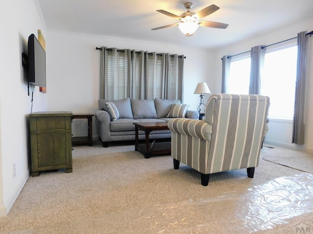 living area featuring light colored carpet, ceiling fan, and baseboards