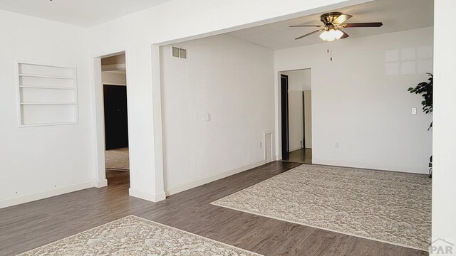 unfurnished room featuring built in shelves, dark wood-style flooring, visible vents, baseboards, and a ceiling fan