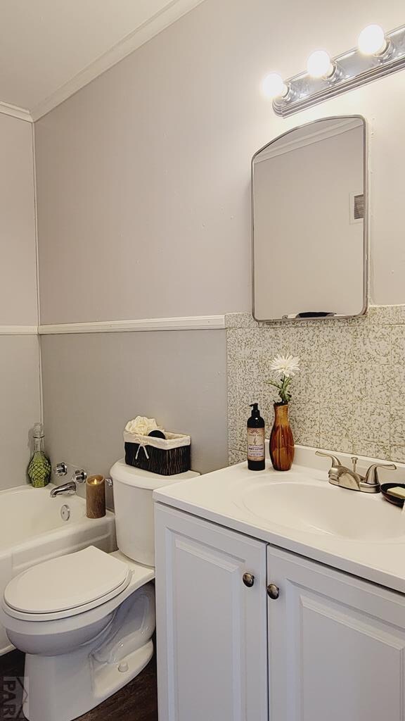 bathroom featuring lofted ceiling, toilet, vanity, ornamental molding, and decorative backsplash