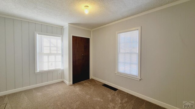 empty room featuring baseboards, visible vents, light colored carpet, a textured ceiling, and crown molding