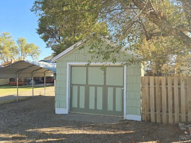 view of outdoor structure with dirt driveway, an outdoor structure, fence, and a detached carport