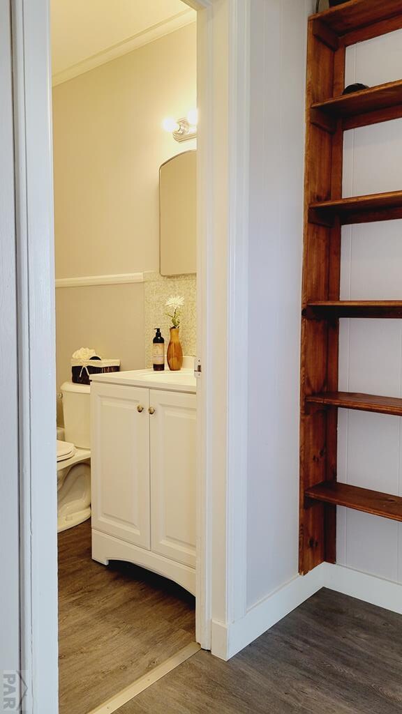 bathroom with decorative backsplash, toilet, ornamental molding, wood finished floors, and vanity