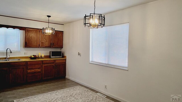 kitchen featuring baseboards, dark floors, decorative light fixtures, light countertops, and a sink