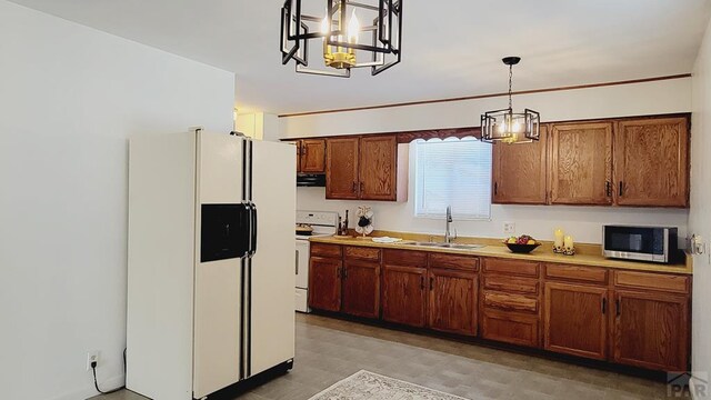 kitchen featuring white appliances, brown cabinets, hanging light fixtures, light countertops, and a sink