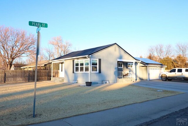 view of front facade with a garage, fence, driveway, roof mounted solar panels, and stucco siding