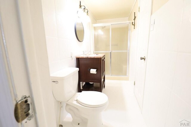 full bath with vanity, a shower stall, toilet, and tile walls