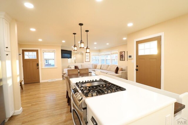 kitchen featuring a center island, stainless steel range with gas cooktop, decorative light fixtures, light countertops, and open floor plan