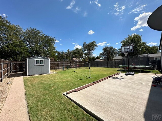 view of yard with a trampoline, an outbuilding, a fenced backyard, and a storage unit