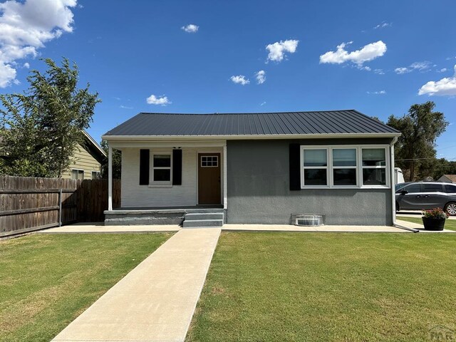 view of front of property with stucco siding, fence, metal roof, and a front yard