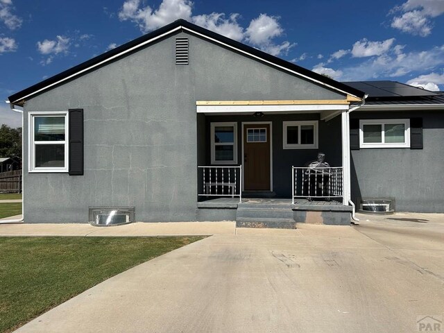 view of front of property featuring a porch, solar panels, and stucco siding