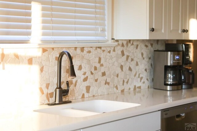 kitchen with a sink, white cabinets, light countertops, stainless steel dishwasher, and backsplash