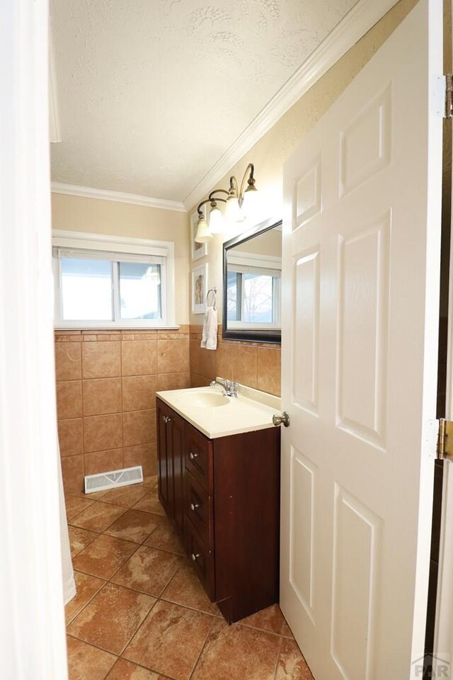 bathroom with a healthy amount of sunlight, vanity, visible vents, and tile walls