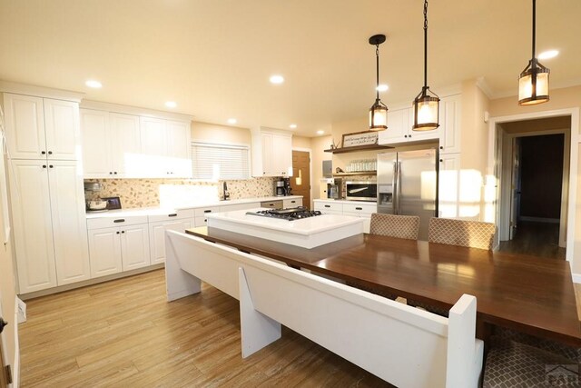 kitchen with hanging light fixtures, appliances with stainless steel finishes, white cabinets, and decorative backsplash