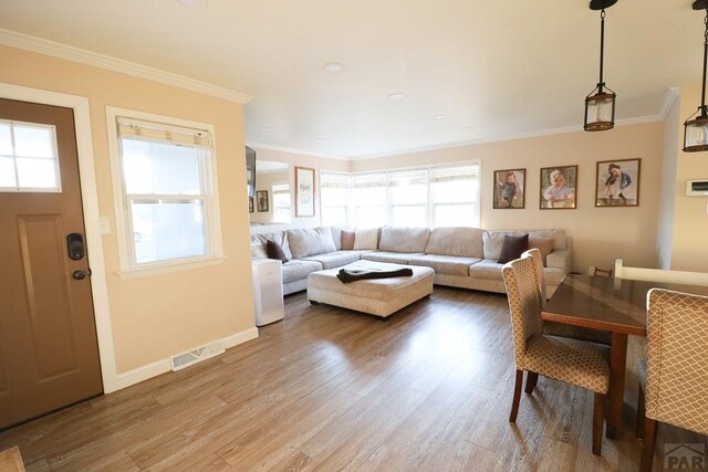 living room with baseboards, wood finished floors, visible vents, and crown molding