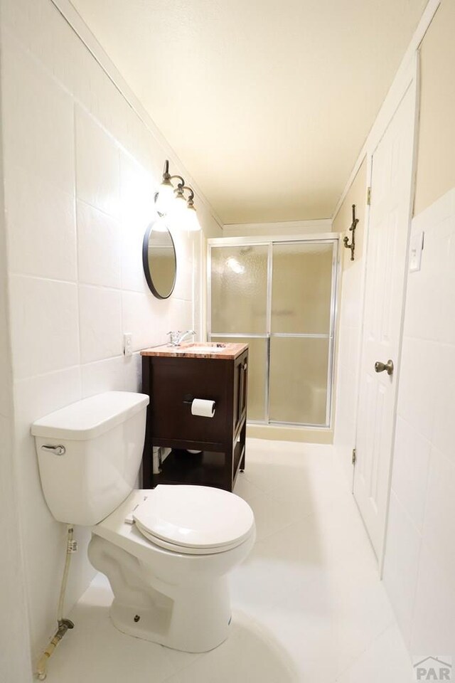 bathroom with tile walls, a shower stall, toilet, and vanity