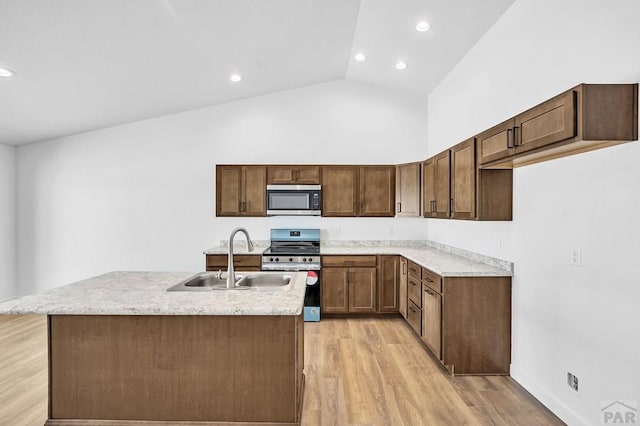 kitchen with a sink, light countertops, appliances with stainless steel finishes, light wood finished floors, and an island with sink