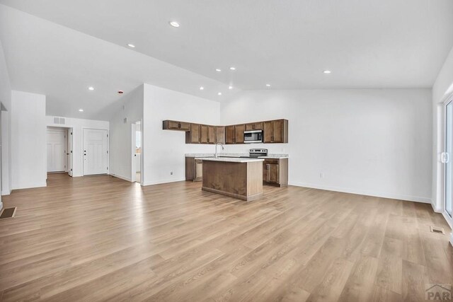 kitchen featuring a kitchen island with sink, open floor plan, light countertops, appliances with stainless steel finishes, and light wood finished floors