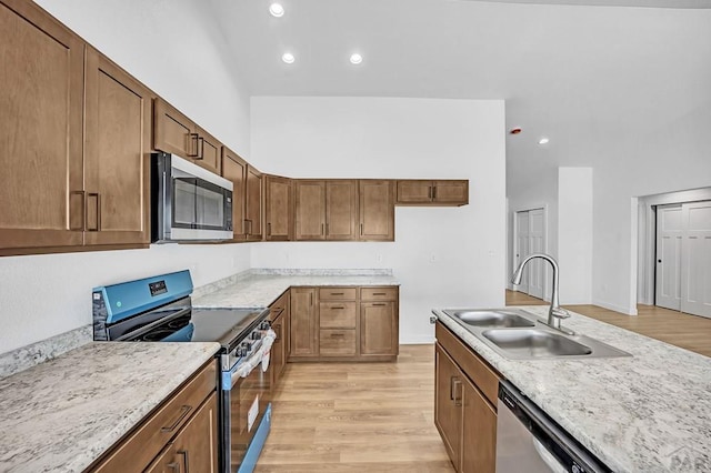 kitchen featuring brown cabinetry, stainless steel appliances, a sink, and light wood finished floors