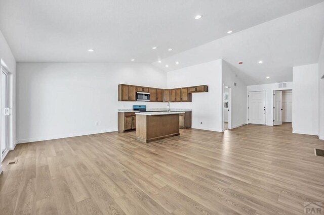 kitchen featuring brown cabinets, open floor plan, a kitchen island with sink, stainless steel appliances, and light countertops