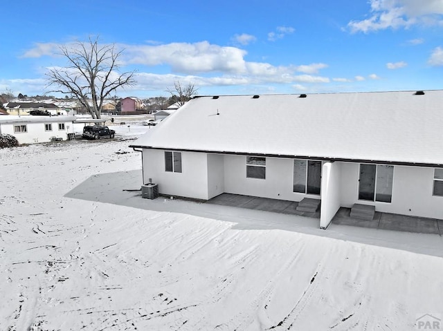 snow covered property featuring entry steps, stucco siding, a patio, and central air condition unit