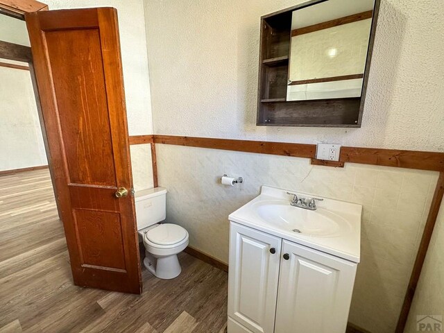 bathroom with a textured wall, vanity, wood finished floors, and toilet