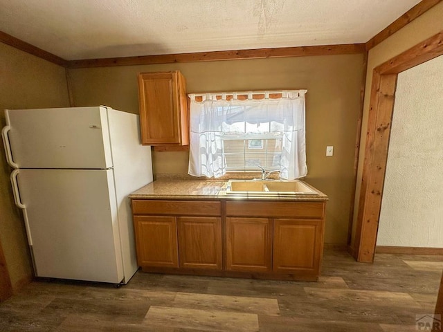 kitchen with dark wood finished floors, light countertops, brown cabinetry, freestanding refrigerator, and a sink