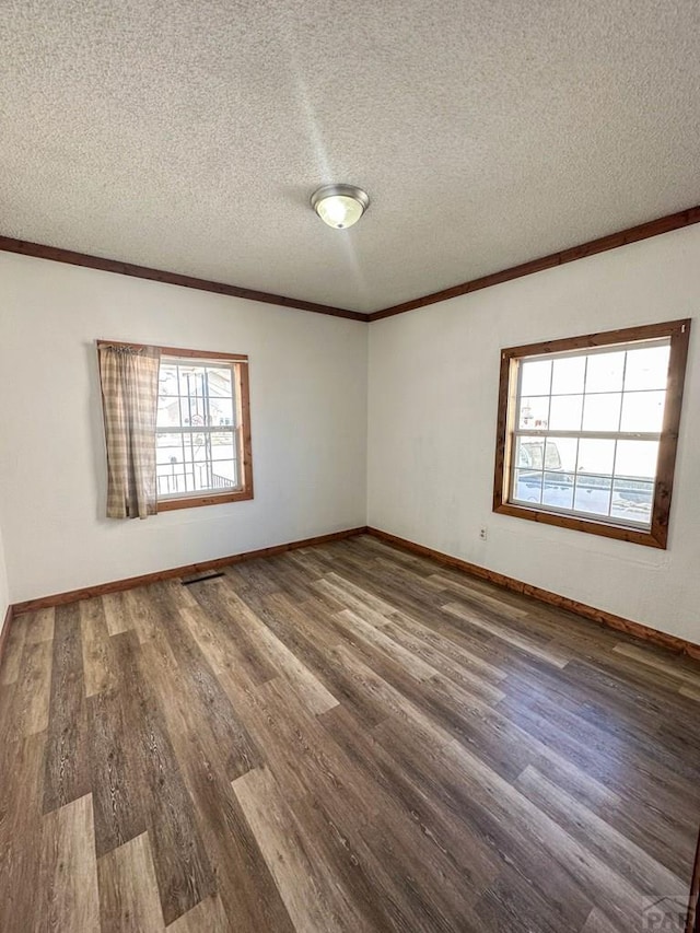 spare room with a textured ceiling, baseboards, wood finished floors, and crown molding