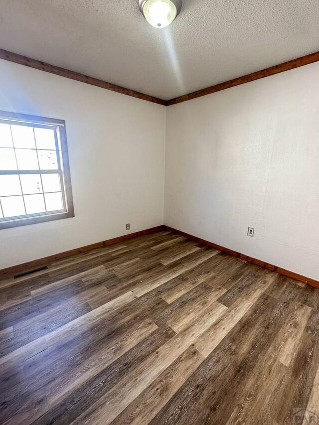 unfurnished room featuring dark wood-style flooring, visible vents, a textured ceiling, and baseboards