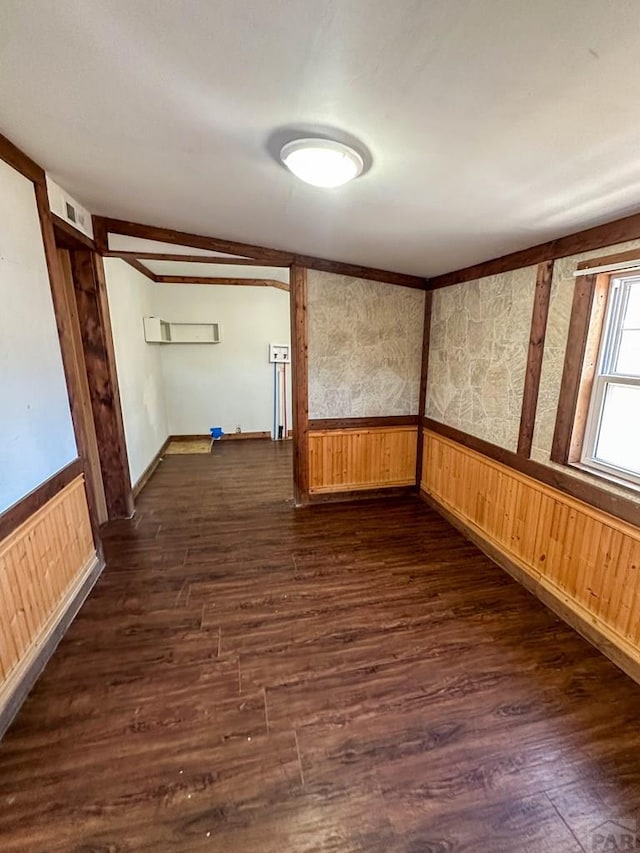 spare room with wooden walls, dark wood-style flooring, a wainscoted wall, and visible vents