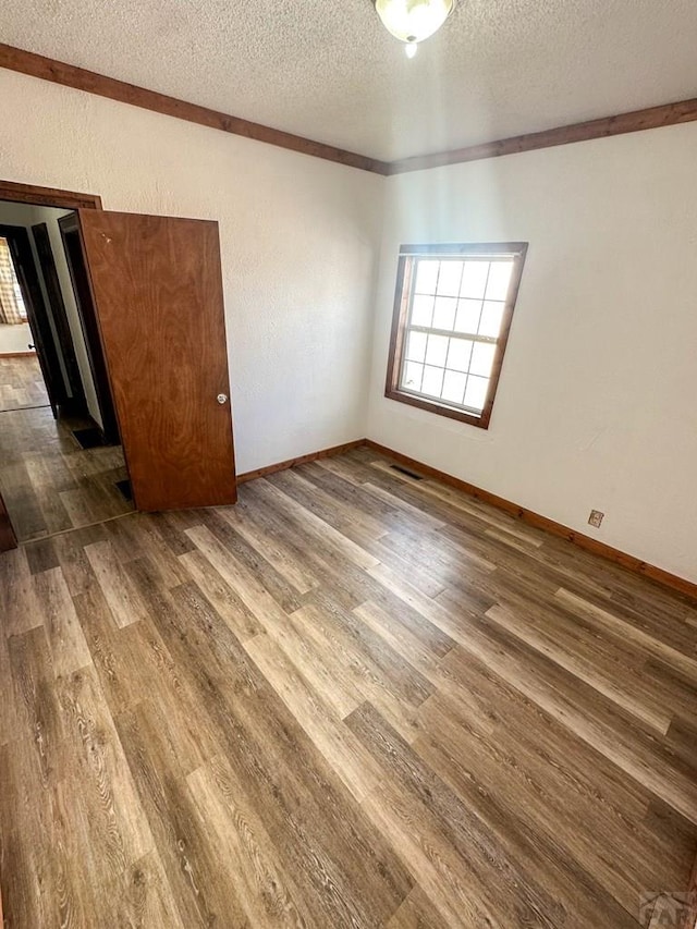 spare room with a textured ceiling, wood finished floors, visible vents, and baseboards